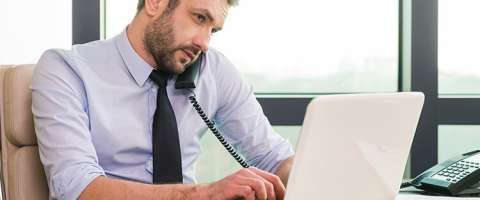 Businessman working on laptop in office while talking on phone