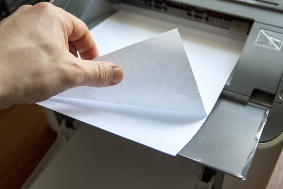 close up of a hand thumbing through paper on the output tray of a printer