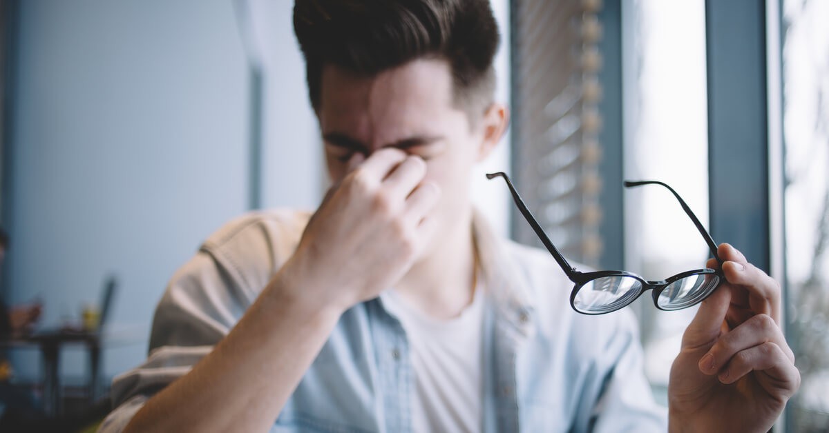 Frustrated employee rubs his eyes and holds his glasses when struggling to determine image resolution