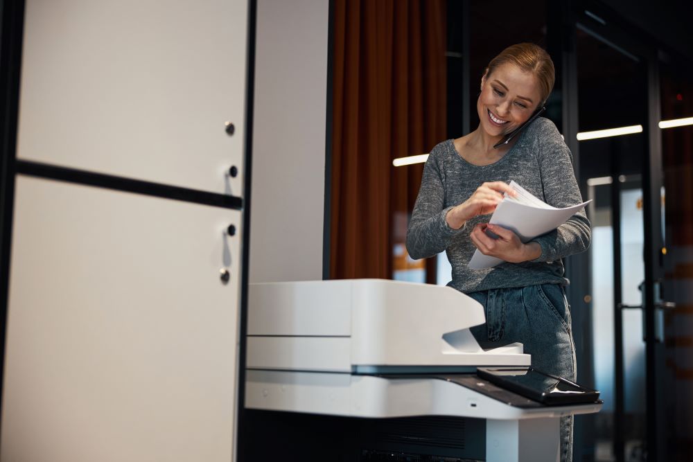 Office professional smiles as going through outputs on one of her office's copiers