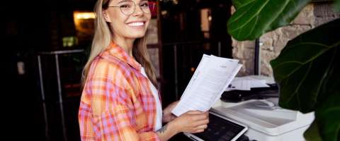 A smiling office worker stands at a color multifunction printer.