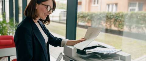 Happy female employee raises the lid on a multifunction printer to make copies symbolizing the importance of copier maintenance.