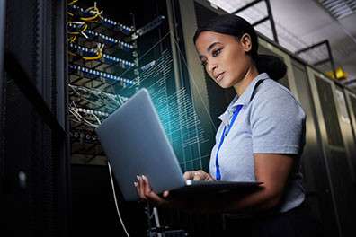 Female IT employee in server room checking something on laptop computer