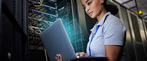 Female IT employee in server room checking something on laptop computer
