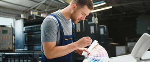 Production printer assistant checking color swatches next to production printer